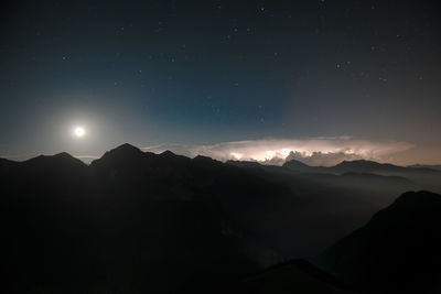 In the night, lightning iin the lower valley, with a starry sky and the moon.