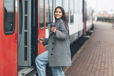 Happy girl enters the train at the station with coffee in her hands