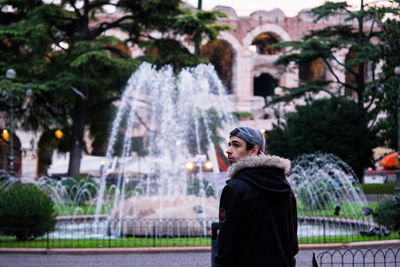 Young man standing by fountain at park