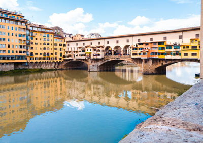 Arch bridge over river by buildings against sky