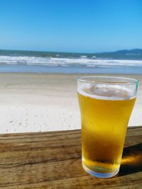 Close-up of beer glass on table against sea at beach