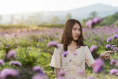 Young woman standing by purple flower on field