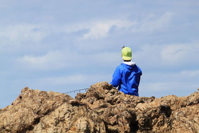Low angle view of man standing on rock against clear blue sky