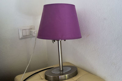 Close-up of electric lamp on table against wall at home