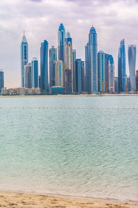 Sea by modern buildings against sky in city