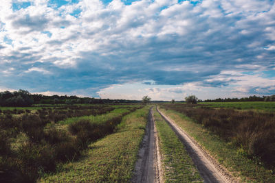 Empty road amidst field against sky