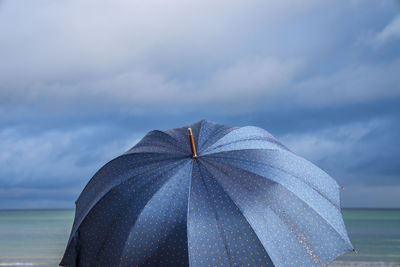Close-up of open umbrella against cloudy sky at beach