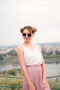 Portrait of young woman wearing sunglasses standing against clear sky