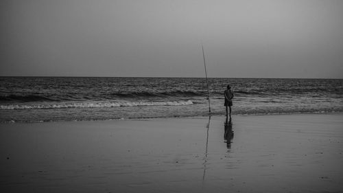 Silhouette man fishing on beach against clear sky