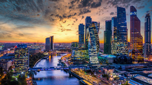 Illuminated buildings in city against sky during sunset