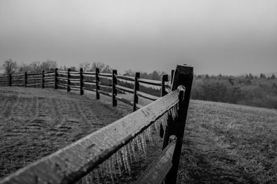 Ice covered wooden fence on field against sky