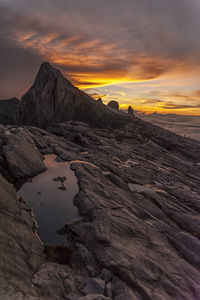 Rock formation by sea against orange sky