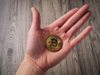 Cropped hand of woman holding bitcoin over table