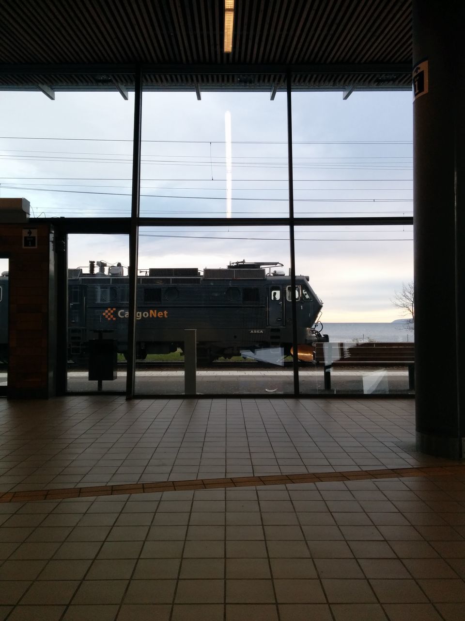 indoors, architecture, built structure, window, glass - material, sky, transparent, building exterior, empty, flooring, reflection, railroad station, transportation, tiled floor, city, sunlight, day, absence, cloud - sky, building