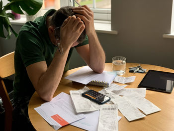 Man is making audit of household expenses using calculator and notebook. lots of receipts and bills