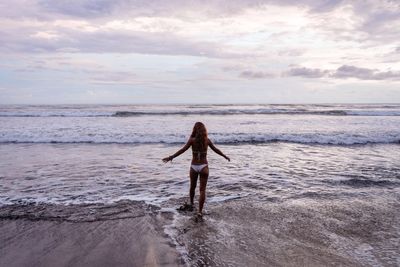 Rear view of woman standing on beach against sky