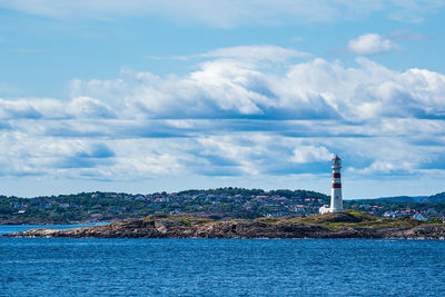 Lighthouse amidst sea and buildings against sky