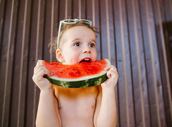 Low angle view of shirtless girl eating watermelon against wall