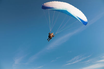 A paraglider takes off from a mountainside with a blue and white canopy and the sun behind. a