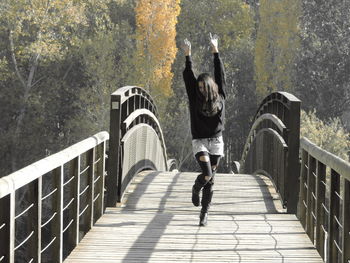 Full length of cheerful woman walking with arms raised on footbridge