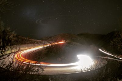 High angle view of light trails on road by mountains against sky at night