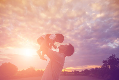 Low angle view of father holding daughter against sky during sunset