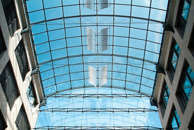 Low angle view of glass ceiling against blue sky