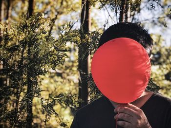 Midsection of person holding balloons against trees