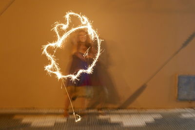 Blurred motion of woman holding illuminated sparkler against wall at night