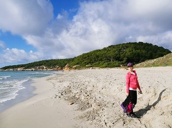 Woman standing on shore at beach against cloudy sky