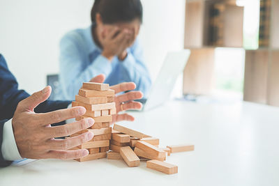 Cropped image of businessman playing block removal game while stressed businesswoman sitting in background at desk