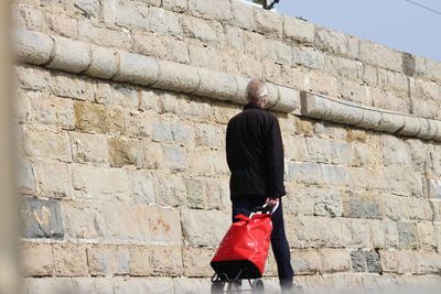 Rear view of man with umbrella walking on brick wall