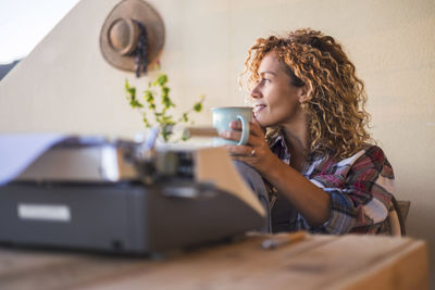 Woman holding coffee cup by typewriter sitting at home