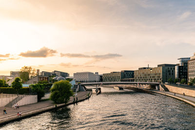 Bridge over river by buildings in city against sky