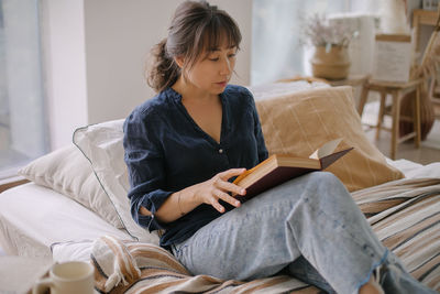 Woman reading book while sitting at home