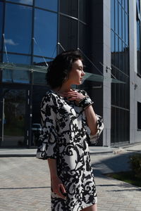 Fashionable young woman wearing floral patterned dress standing against building in city