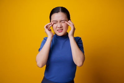 Young woman standing against yellow background