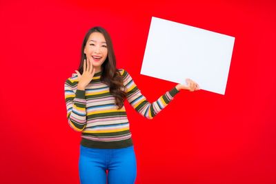 Portrait of a smiling young woman standing against red background