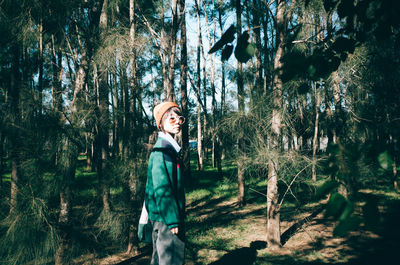 Man standing by tree trunk in forest