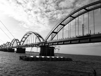 Black and whitephoto of a bridge over river against cloudy sky 