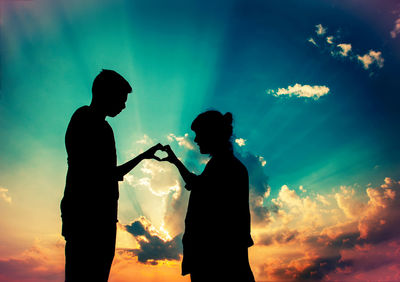 Low angle view of silhouette couple making heart shape against sky