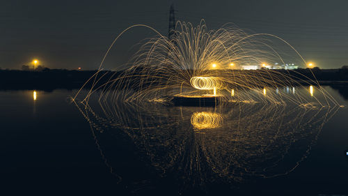 Light trails over river against sky at night