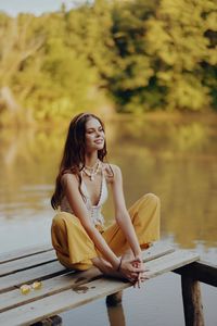 Young woman sitting on pier over lake