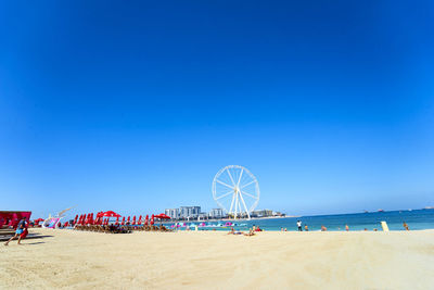 People at beach against clear blue sky during summer