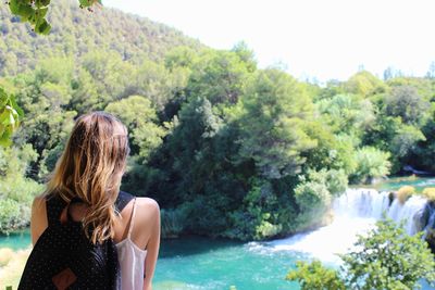 Woman standing by river against trees