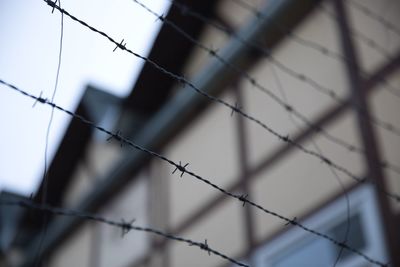 Barbed wire fence strings with house in blurred background. focus on foreground. low angle view.