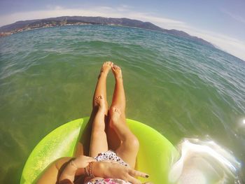 Low section of mother with daughter relaxing in sea against sky