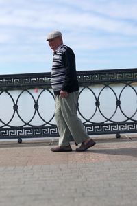 Side view of man standing by railing against sky