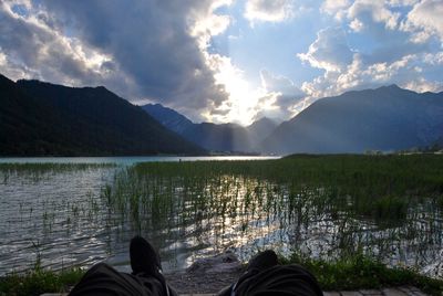 Low section of man at lake against cloudy sky