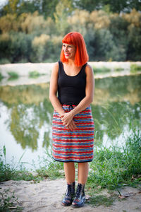 Full length of smiling woman looking away while standing by lake